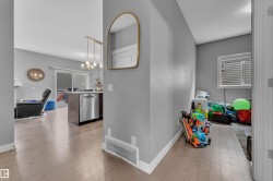 Open-concept living area featuring light wood-finish flooring, a contemporary island with a built-in dishwasher, and a multi-pendant light fixture - 