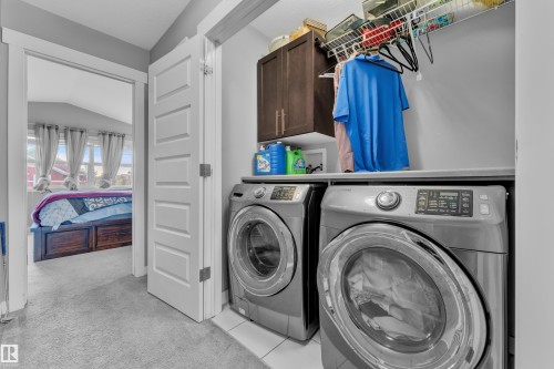 Dedicated laundry space featuring front-loading machines, built-in shelving, and upper cabinetry - 1942 Chapman Road Sw, Edmonton, AB - Indoor Photo Showing Laundry Room