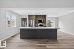 Modern kitchen featuring a central island with a light-colored countertop, stainless steel appliances, two-tone cabinetry, wood-finish flooring, and recessed lighting - 