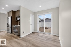 Open-concept living area with wood-finish flooring, a contemporary kitchen featuring stainless steel appliances and brown cabinetry, and a sliding glass door opening to an outdoor paver patio - 