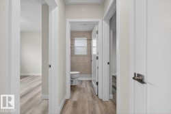 Hallway featuring light wood-finish flooring, white paneled doors, and contemporary door hardware - 