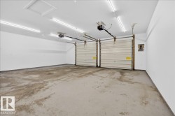 Two-car garage featuring segmented overhead doors with openers, exposed ceiling joists, and fluorescent strip lighting - 