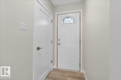Entryway featuring a paneled white door with an arched glass insert, a second white door with brushed nickel hardware, light wood-finish flooring, and light-toned walls - 