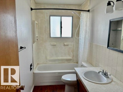 Bathroom featuring a bathtub with an integrated shower, white wall-mounted sink, light-toned countertop, and wood-finish flooring - 5206 51Ave, Willingdon, AB - Indoor Photo Showing Bathroom