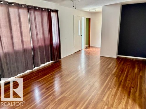 Spacious room featuring wood-finish flooring, white baseboards, and a black accent wall - 5206 51Ave, Willingdon, AB - Indoor Photo Showing Other Room
