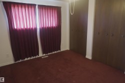 Room featuring dark wood-finish bi-fold closet doors, wall-to-wall carpeting, and white baseboards - 