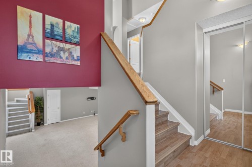Multi-level interior featuring wood-finish flooring, light grey wall paint, white baseboards, and a wood handrail - 3211 Mcphadden Place Sw, Edmonton, AB - Indoor Photo Showing Other Room