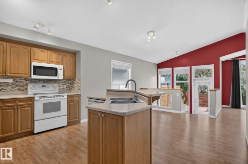 Kitchen featuring wood cabinetry, white appliances, and a mosaic tile backsplash - 3211 Mcphadden Place Sw, Edmonton, AB - Indoor Photo Showing Kitchen With Double Sink
