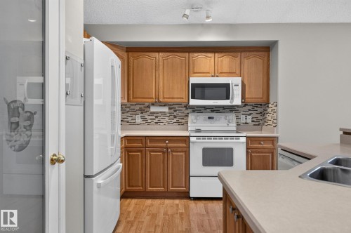 Kitchen featuring wood-finish cabinetry, white appliances, and a mosaic tile backsplash - 3211 Mcphadden Place Sw, Edmonton, AB - Indoor Photo Showing Kitchen With Double Sink