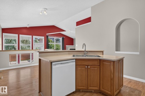 Kitchen island featuring a dual-basin stainless steel sink with a high-arc faucet, light-toned countertop, and wood cabinetry - 3211 Mcphadden Place Sw, Edmonton, AB - Indoor Photo Showing Kitchen With Double Sink
