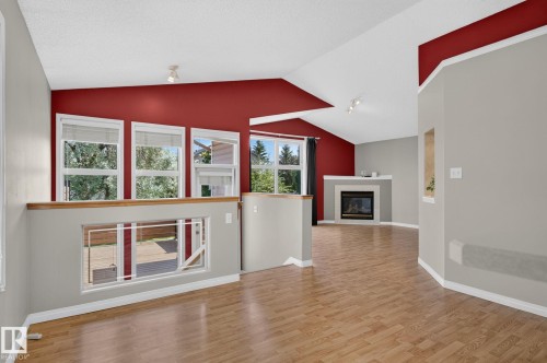 Living area featuring wood-finish flooring, a fireplace with a white mantel, vaulted ceilings, and multiple windows - 3211 Mcphadden Place Sw, Edmonton, AB - Indoor With Fireplace