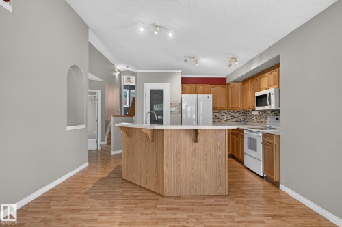 Kitchen featuring a wood-finish island with integrated sink, light-toned countertops, and a mosaic tile backsplash - 3211 Mcphadden Place Sw, Edmonton, AB - Indoor Photo Showing Kitchen