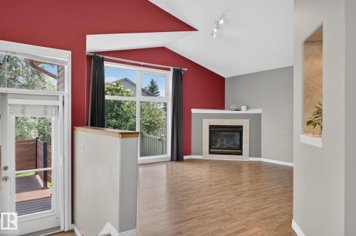 Spacious living area featuring wood-finish flooring, a corner fireplace with a tiled surround, and large windows - 3211 Mcphadden Place Sw, Edmonton, AB - Indoor Photo Showing Living Room With Fireplace