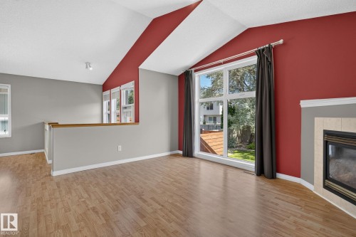 Vaulted ceiling with track lighting, wood-finish flooring, half-wall partition with wood cap, large picture window, and fireplace with tile surround - 3211 Mcphadden Place Sw, Edmonton, AB - Indoor With Fireplace