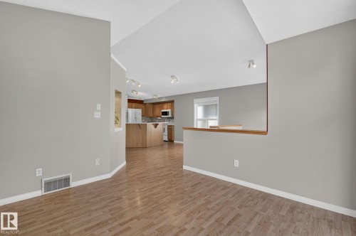 Open-concept interior featuring wood-finish flooring, a kitchen with light wood cabinetry and stainless steel appliances, and grey wall tones - 3211 Mcphadden Place Sw, Edmonton, AB - Indoor