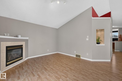 Living room featuring a corner fireplace with a tile surround and mantel, wood-finish flooring, vaulted ceilings, and track lighting - 3211 Mcphadden Place Sw, Edmonton, AB - Indoor With Fireplace
