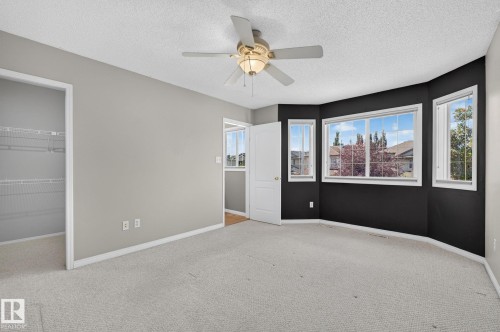 Carpeted room featuring a ceiling fan with light fixture, bay windows, a solid panel interior door, and a closet with wire shelving - 3211 Mcphadden Place Sw, Edmonton, AB - Indoor Photo Showing Other Room