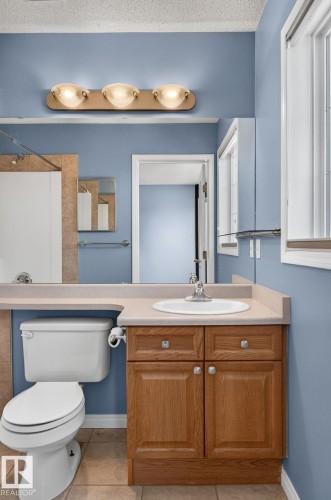 Bathroom vanity featuring a light-toned countertop with an integrated sink, oak-finish cabinetry, and a three-light fixture - 3211 Mcphadden Place Sw, Edmonton, AB - Indoor Photo Showing Bathroom