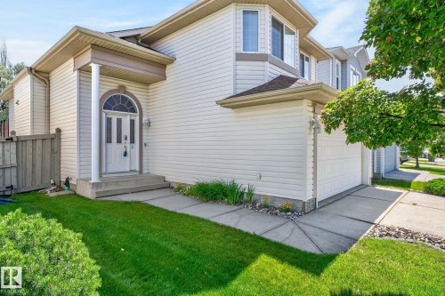Exterior featuring light-colored siding, an arched transom window above the main entry, a covered porch with a column, an attached garage, and a bay window on the upper level - 3211 Mcphadden Place Sw, Edmonton, AB - Outdoor