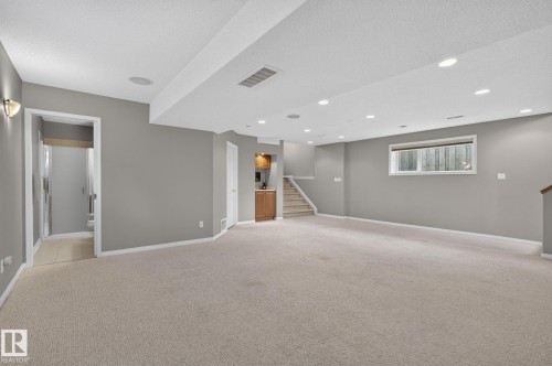 Spacious lower-level room featuring recessed lighting, a built-in wet bar with wood-finish cabinetry, a window with horizontal blinds, and access to a tiled bathroom - 3211 Mcphadden Place Sw, Edmonton, AB - Indoor