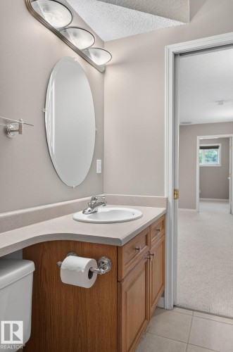 Vanity area featuring a light-colored countertop, an oval-shaped mirror, and a three-light fixture - 3211 Mcphadden Place Sw, Edmonton, AB - Indoor Photo Showing Bathroom