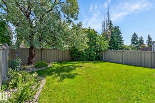 Grassed backyard featuring mature trees, surrounding privacy fencing, and garden beds with integrated landscape lighting - 3211 Mcphadden Place Sw, Edmonton, AB - Outdoor With Backyard