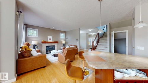 Open-concept living area featuring wood-finish flooring, a contemporary fireplace with tile surround, and a kitchen island with a stone-finish countertop - 335 62 Street Sw, Edmonton, AB - Indoor Photo Showing Living Room With Fireplace