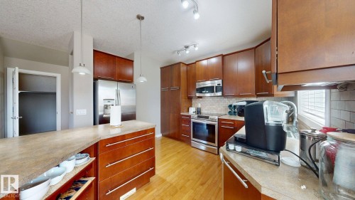 Spacious kitchen featuring stainless steel appliances, abundant wood cabinetry, a large center island with pendant lighting, stone countertops, and wood-finish flooring - 335 62 Street Sw, Edmonton, AB - Indoor Photo Showing Kitchen