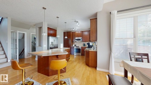 Open-concept kitchen with wood-finish flooring, cherry wood cabinetry, and stainless steel appliances - 335 62 Street Sw, Edmonton, AB - Indoor