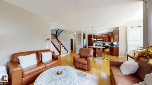 Open-concept living space featuring wood-finish flooring, a kitchen with dark wood cabinetry and an island, stainless steel appliances, and a carpeted staircase with wood railings - 335 62 Street Sw, Edmonton, AB - Indoor Photo Showing Living Room