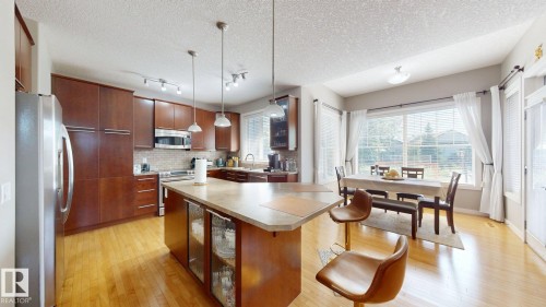 Open-concept kitchen and dining area featuring rich wood cabinetry, stainless steel appliances, a center island with integrated glass-front display cabinets, light-toned countertops, and hardwood flooring - 335 62 Street Sw, Edmonton, AB - Indoor Photo Showing Other Room