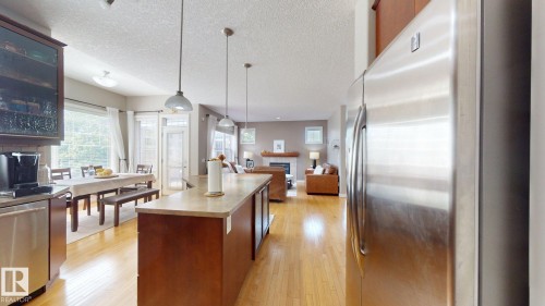 Open-concept kitchen and dining area featuring a central island with countertop, wood-finish flooring, stainless steel appliances, and a dining space with a large window - 335 62 Street Sw, Edmonton, AB - Indoor Photo Showing Kitchen