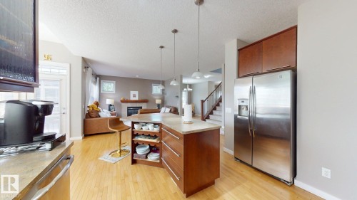 Open-concept kitchen featuring an island with built-in shelving, pendant lighting, wood-finish flooring, and stainless steel appliances - 335 62 Street Sw, Edmonton, AB - Indoor