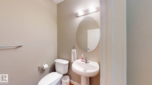 Pedestal sink with chrome faucet, an oval mirror, and overhead vanity lighting - 335 62 Street Sw, Edmonton, AB - Indoor Photo Showing Bathroom