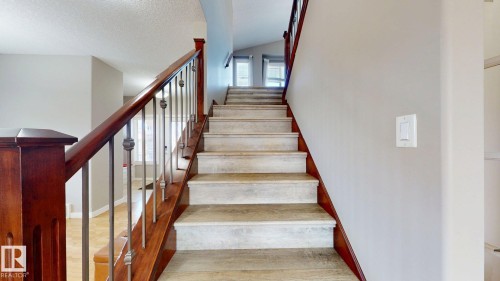 Staircase featuring wood-finish treads and risers, complemented by a rich wood-finish handrail with decorative metal balusters - 335 62 Street Sw, Edmonton, AB - Indoor Photo Showing Other Room