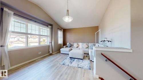 Living room featuring light wood-finish flooring, a vaulted ceiling, and multiple windows with white trim - 335 62 Street Sw, Edmonton, AB - Indoor