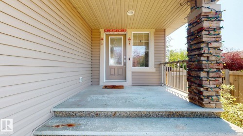 Covered concrete front porch with textured stone pillar, light-toned siding, and a glass-paneled entry door - 335 62 Street Sw, Edmonton, AB - Outdoor With Exterior