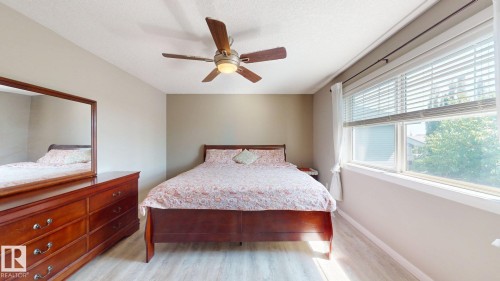Bedroom featuring light wood-finish flooring, a contemporary ceiling fan, and a large window with white blinds and drapes - 335 62 Street Sw, Edmonton, AB - Indoor Photo Showing Bedroom
