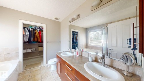 Dual vanity with integrated sinks, a built-in jetted tub, tiled flooring, and a walk-in closet with shelving and hanging rods - 335 62 Street Sw, Edmonton, AB - Indoor Photo Showing Bathroom