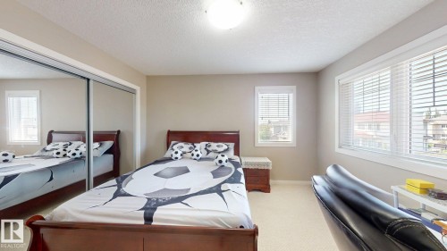 Bedroom featuring a spacious mirrored sliding closet, two windows with blinds, and light-toned carpet flooring - 335 62 Street Sw, Edmonton, AB - Indoor Photo Showing Bedroom