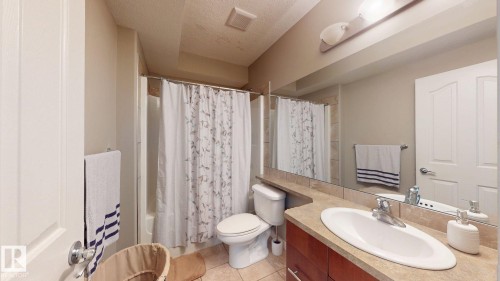 Full bathroom featuring a single vanity with a neutral-toned countertop, integrated basin, and wood-finish cabinetry - 335 62 Street Sw, Edmonton, AB - Indoor Photo Showing Bathroom