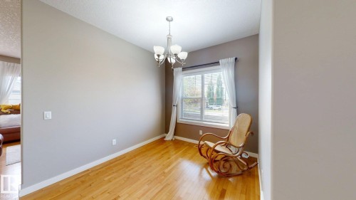 Spacious room with wood-finish flooring, a contemporary chandelier, and a large window with blinds - 335 62 Street Sw, Edmonton, AB - Indoor Photo Showing Other Room