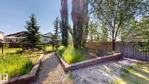 Landscaped backyard featuring a gravel path, modular block retaining walls, mature trees, and a wood privacy fence - 335 62 Street Sw, Edmonton, AB - Outdoor
