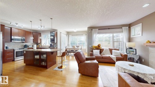 Open-concept living space featuring wood-finish flooring, a kitchen island with pendant lighting, stainless steel appliances, a tile backsplash, and multiple windows - 335 62 Street Sw, Edmonton, AB - Indoor