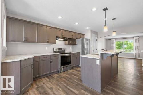 Kitchen featuring modern gray cabinetry, stainless steel appliances, light speckled countertops, and wood-finish flooring - 1627 167 Street Sw, Edmonton, AB - Indoor Photo Showing Kitchen With Upgraded Kitchen