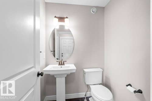 Pedestal sink with bronze-finish faucet, oval mirror, and overhead lighting fixture - 1627 167 Street Sw, Edmonton, AB - Indoor Photo Showing Bathroom