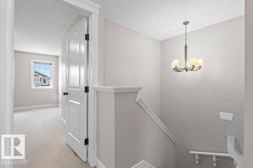 Contemporary chandelier illuminating the stairwell, featuring a neutral color palette, white trim work, and a paneled interior door - 1627 167 Street Sw, Edmonton, AB - Indoor Photo Showing Other Room