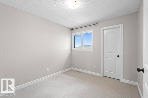 Carpeted room featuring a white interior door with black hardware, a window with white trim, light gray walls, and white baseboards - 1627 167 Street Sw, Edmonton, AB - Indoor Photo Showing Other Room