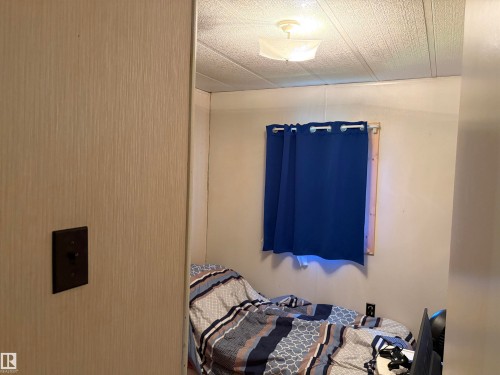 Room featuring a window with blue curtains, textured wall paneling, and a ceiling light fixture - # 501  11131 Twp Rd 600, Rural St. Paul County, AB - Indoor Photo Showing Bedroom