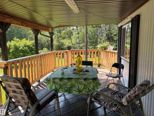 Covered wooden porch featuring a wood railing, exposed wood beams, a dark wood-finish floor, and a metal ceiling - # 501  11131 Twp Rd 600, Rural St. Paul County, AB - Outdoor With Deck Patio Veranda With Exterior